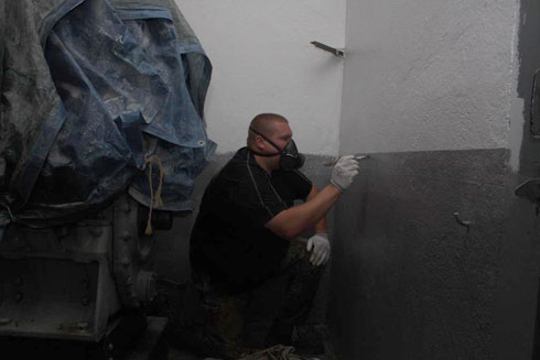 Eric qui applique la couche de gris sur le soubassement du mur.